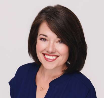 Woman with a brunette bob wearing a blue top, smiling to the camera in front of a white background